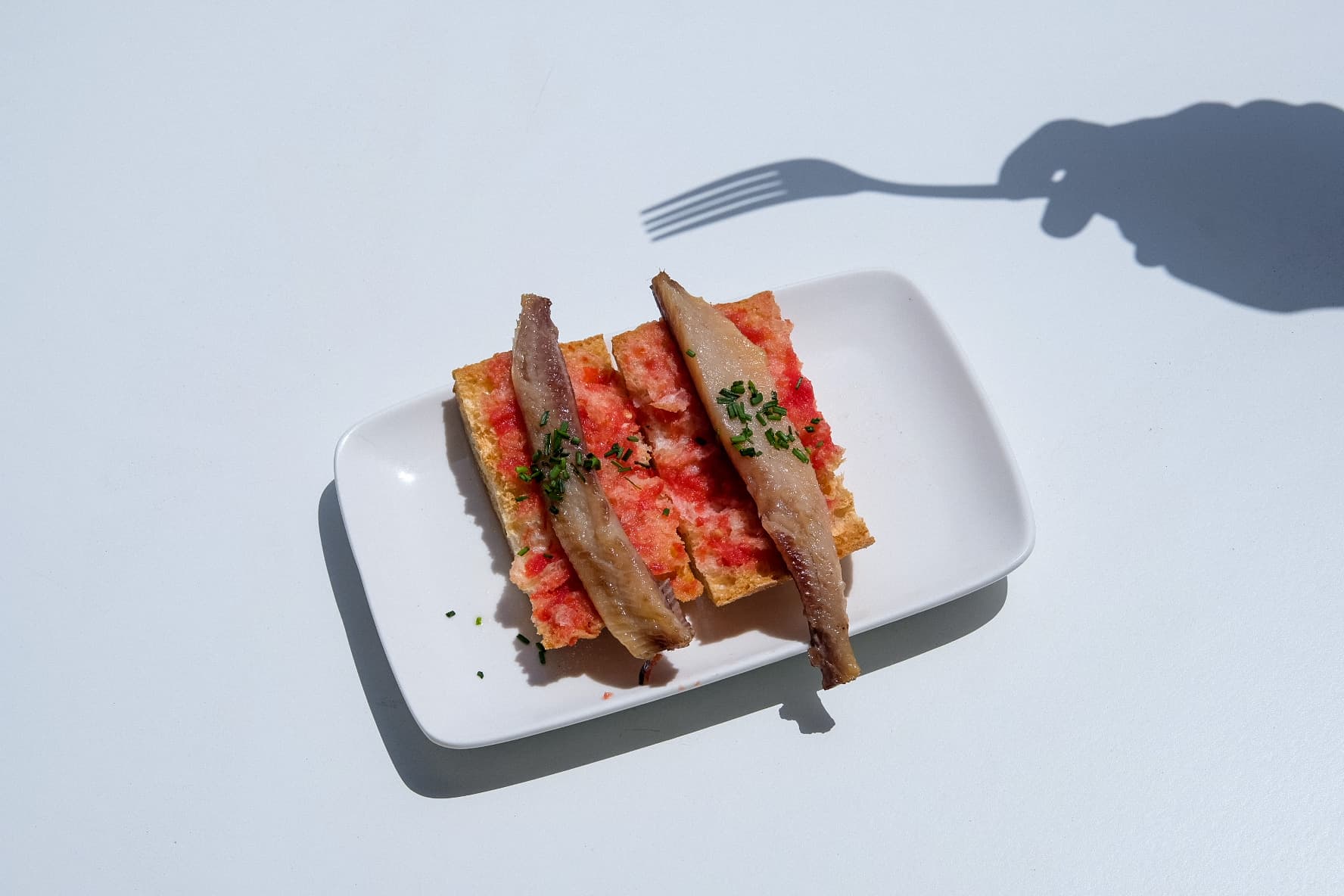 Anchovy toast with a hand-and-fork shadow
